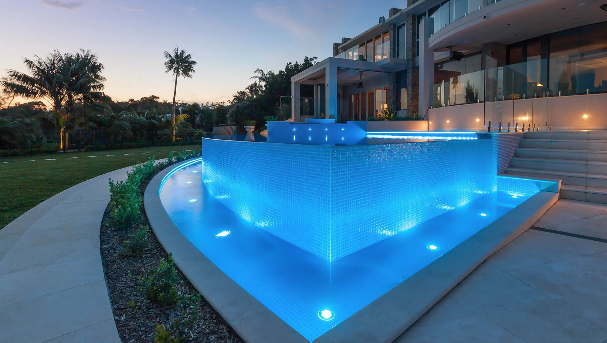 Concrete pool with a tiled infinity wall lit at dusk beside a Cronulla home